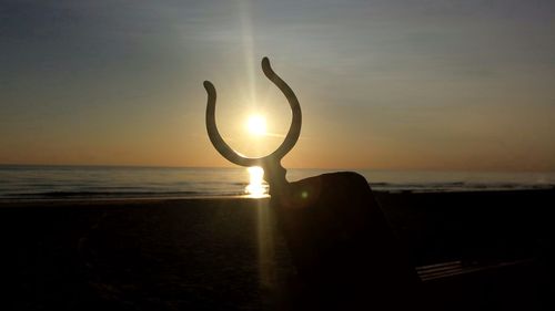 Silhouette beach by sea against sky during sunset