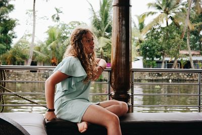 Young woman sitting on railing against lake