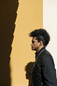 Mid adult man standing sideways by wall during sunny day