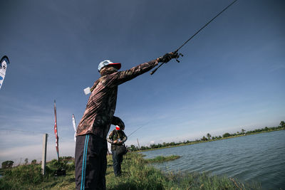 View of people by lake fishing against sky