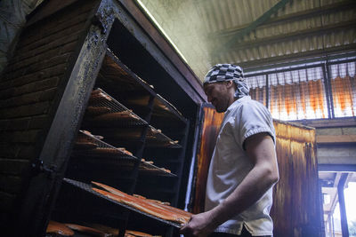 Manual worker inserting fish tray in smokehouse at food factory