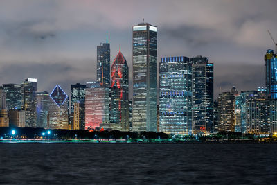 Sea by illuminated buildings against sky