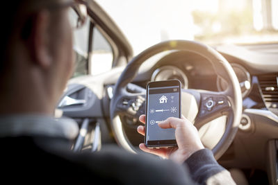 Man in car adjusting devices at home via smartphone