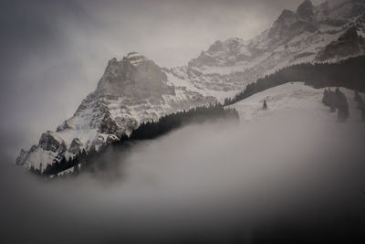 Low angle view of snowcapped mountains against sky in foggy weather