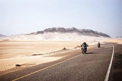 Rear view of people riding motorcycle on desert