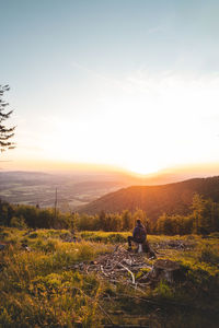 Rear view of man walking on field against sky during sunset