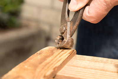 Close-up of human hand removing rusty nail from wood