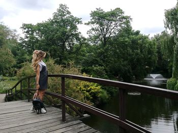 Woman standing on footbridge over river against trees