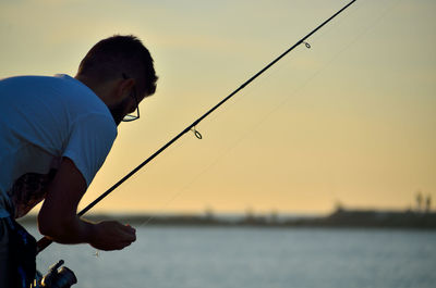 Side view of man fishing in sea against sky