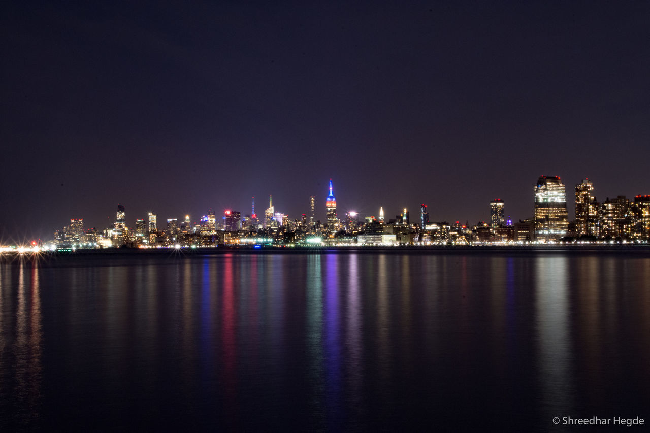 CITY LIT UP AT WATERFRONT AT NIGHT