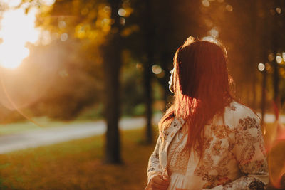 Rear view of woman standing against trees in sunset