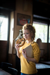 Portrait of smiling woman holding pretzel and tablet at cafe