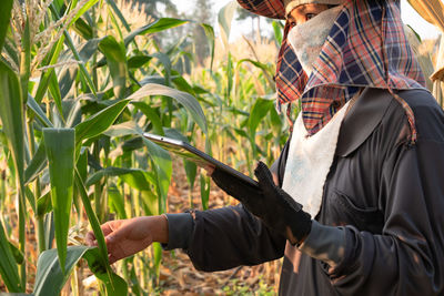 Side view of farmer with digital tablet examining crop leaves at farm