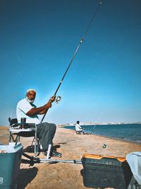 Man fishing by sea against clear blue sky