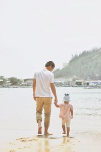 Rear view of father and daughter walking at beach