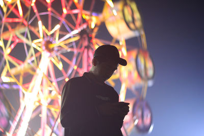 Low angle view of man standing against illuminated lights at night