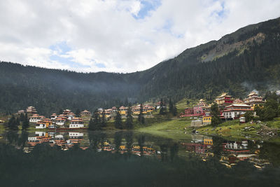 Scenery view of old buildings of tibetan buddhist temples located on shore of tranquil reflecting lake in highland covered with clouds