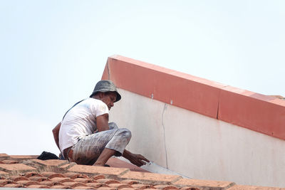 Man sitting against wall against clear sky