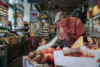 Senior man checking quality of fruit while shopping with grandson in supermarket