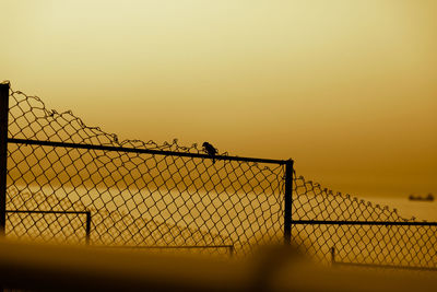 Silhouette chainlink fence against clear sky during sunset