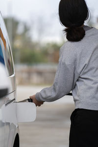 Rear view of woman in sport clothes refuelling the car