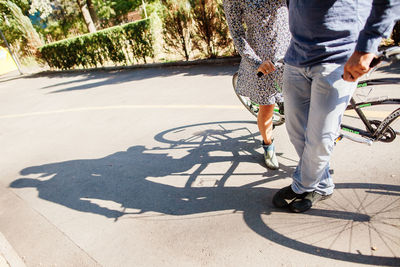 Low section of couple standing with tandem bicycle on road