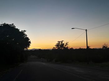 Road by silhouette trees against sky during sunset