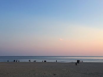 People on beach against clear sky during sunset