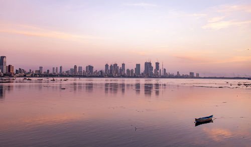 Scenic view of sea by buildings against sky during sunset