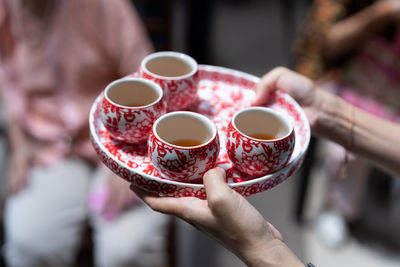 Cropped hands of woman holding tea cups in plate
