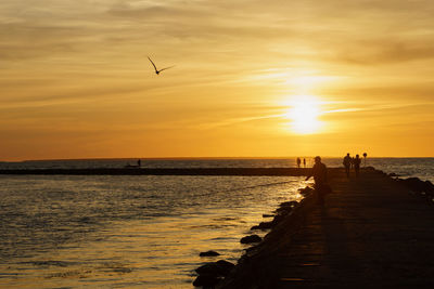 People on jetty by sea at dusk