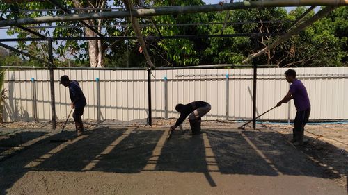 Men cleaning land against fence