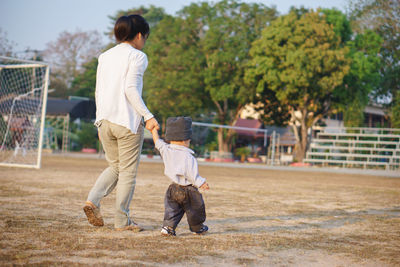 Rear view full length of woman walking with son on soccer field