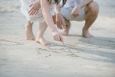 Low section of couple writing on sand at beach