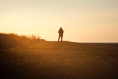 Rear view of silhouette man walking on field against sky