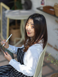 Portrait of smiling young woman using digital tablet while sitting in cafe