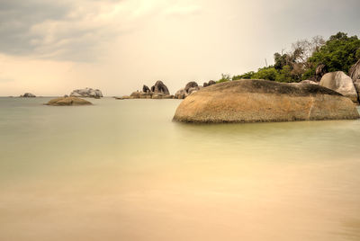 Rocks in sea against cloudy sky during sunset