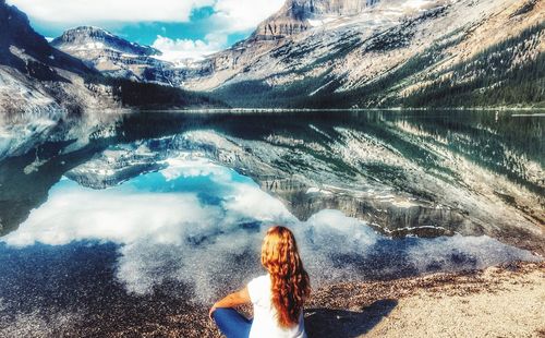 Rear view of woman sitting by lake against mountains