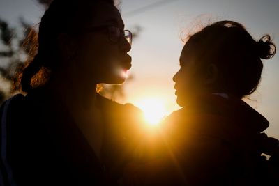 Close-up of mother and daughter against sky during sunset