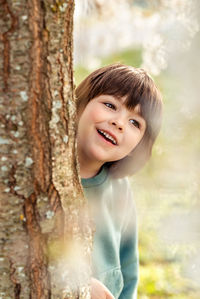 Outdoor portrait of smiling happy toddler boy playing hide and seek hiding behind the tree in park