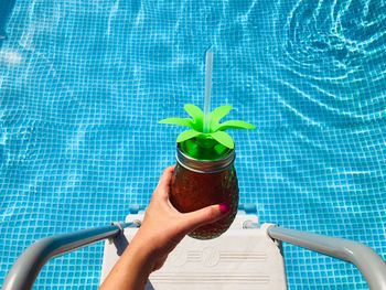 Cropped hand of woman holding drink over swimming pool