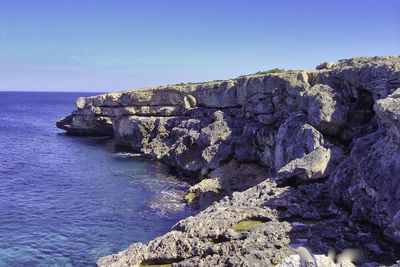 Rocks by sea against clear blue sky