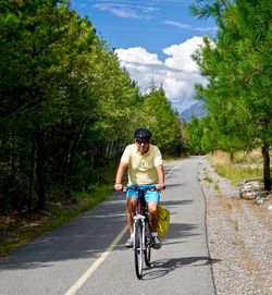 Senior man riding bicycle on road amidst trees during sunny day