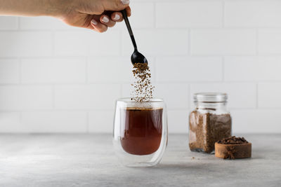 Woman stirs instant coffee in glass mug with boiled water on grey stone table