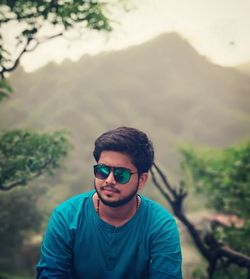 Portrait of young man wearing sunglasses against mountains