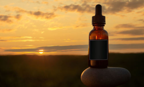 Close-up of glass bottle on table against sky during sunset