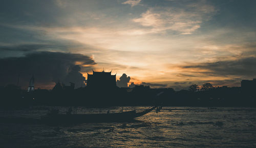 Silhouette buildings by sea against sky during sunset