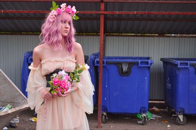 Portrait of young woman standing by plants against the backdrop of trash