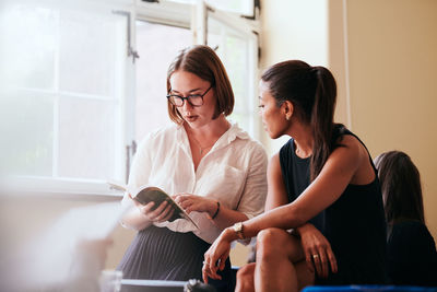 Young woman using smart phone while sitting on laptop