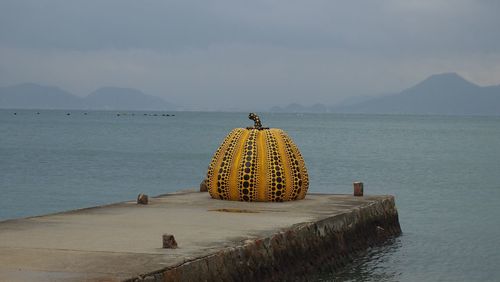 Artificial pumpkin on jetty against cloudy sky